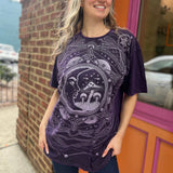A woman wearing the Purple Mushroom Stonewashed Cotton T-shirt with jeans in front of a pink and orange wall.