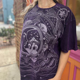 A woman wearing the Purple Mushroom Stonewashed Cotton T-shirt with jeans in front of a pink and orange wall.