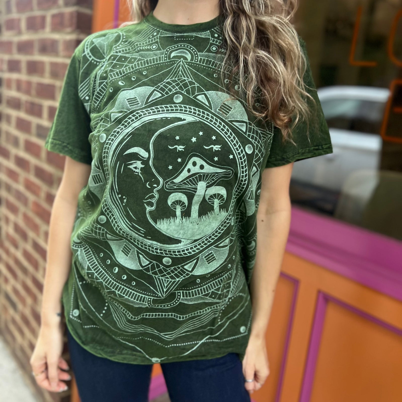 A woman wearing the Green Moon Mushroom Stonewash T-shirt in front of a brick wall.