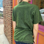 A woman wearing the Green Moon Mushroom Stonewash T-shirt in front of a brick wall.
