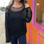 A woman wearing the black Hollow Out Knit Drop Sleeve Sweater in front of a pink and orange wall.