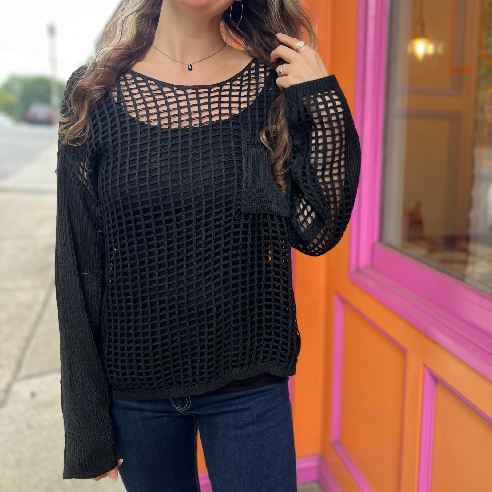 A woman wearing the black Hollow Out Knit Drop Sleeve Sweater in front of a pink and orange wall.