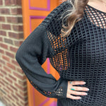 A woman wearing the black Hollow Out Knit Drop Sleeve Sweater in front of a pink and orange wall.