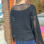 A woman wearing the black Hollow Out Knit Drop Sleeve Sweater in front of a pink and orange wall.