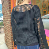 A woman wearing the black Hollow Out Knit Drop Sleeve Sweater in front of a pink and orange wall.