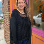 A woman wearing the black Hollow Out Knit Drop Sleeve Sweater in front of a pink and orange wall.
