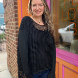 A woman wearing the black Hollow Out Knit Drop Sleeve Sweater in front of a pink and orange wall.