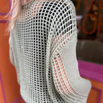 A woman wearing the green Hollow Out Knit Drop Sleeve Sweater in front of a pink and orange wall.