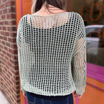 A woman wearing the green Hollow Out Knit Drop Sleeve Sweater in front of a pink and orange wall.