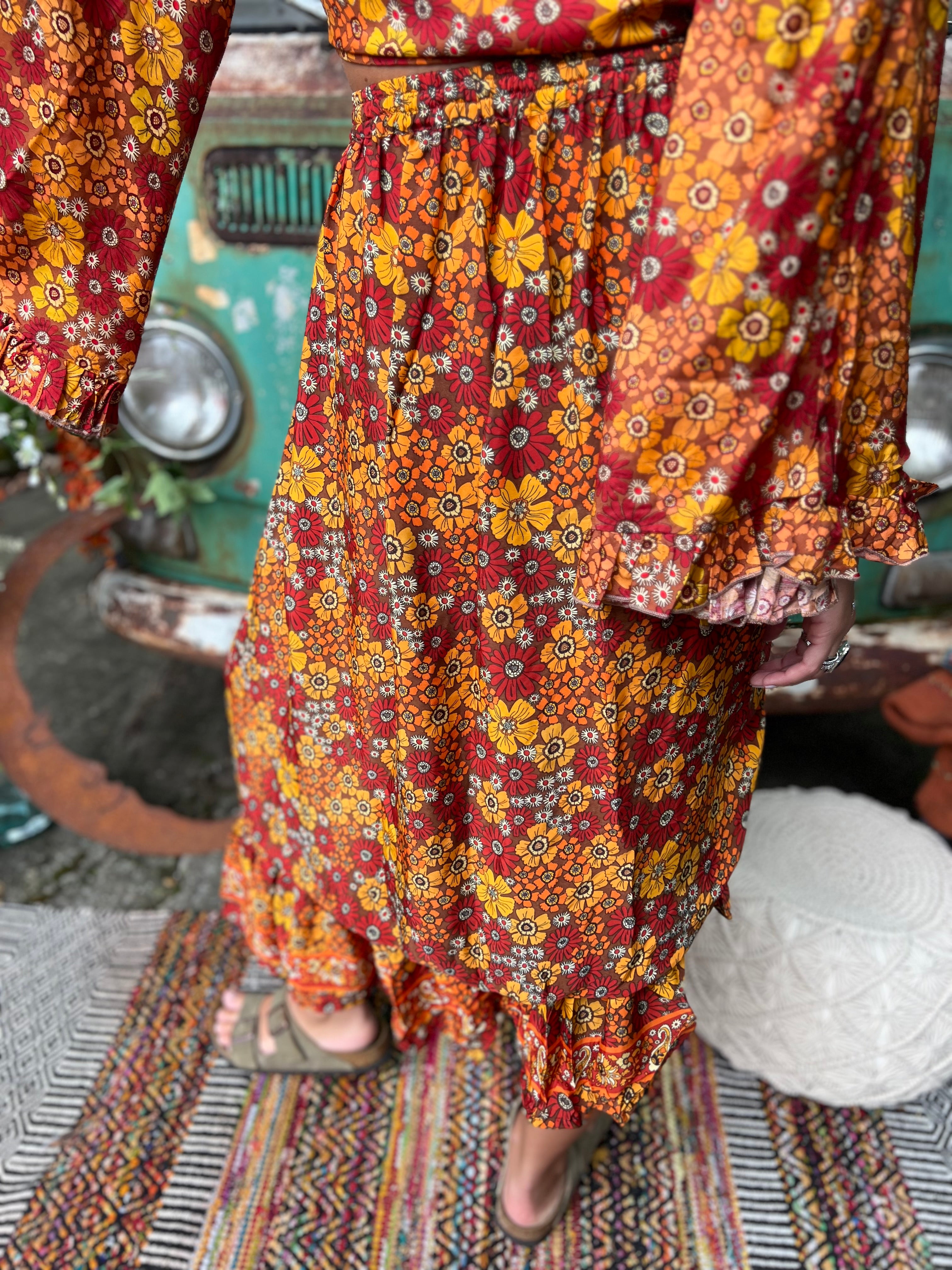 Someone wearing the red Hippie Floral Cinch Maxi Ruffle Skirt in front of a Volkswagen bus.