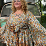 A woman wearing the orange and cream Hippie Bohemian Bell Sleeve Wrap Top with black pants in front of a rusted vintage Volkswagen bus.