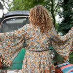 A woman wearing the orange and cream Hippie Bohemian Bell Sleeve Wrap Top with black pants in front of a rusted vintage Volkswagen bus.