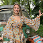 A woman wearing the orange and cream Hippie Bohemian Bell Sleeve Wrap Top with black pants in front of a rusted vintage Volkswagen bus.