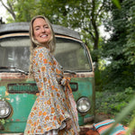 A woman wearing the orange and cream Hippie Bohemian Bell Sleeve Wrap Top with black pants in front of a rusted vintage Volkswagen bus.