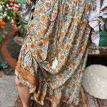 Someone wearing the orange & cream Hippie Floral Cinch Maxi Ruffle Skirt in front of a Volkswagen bus.