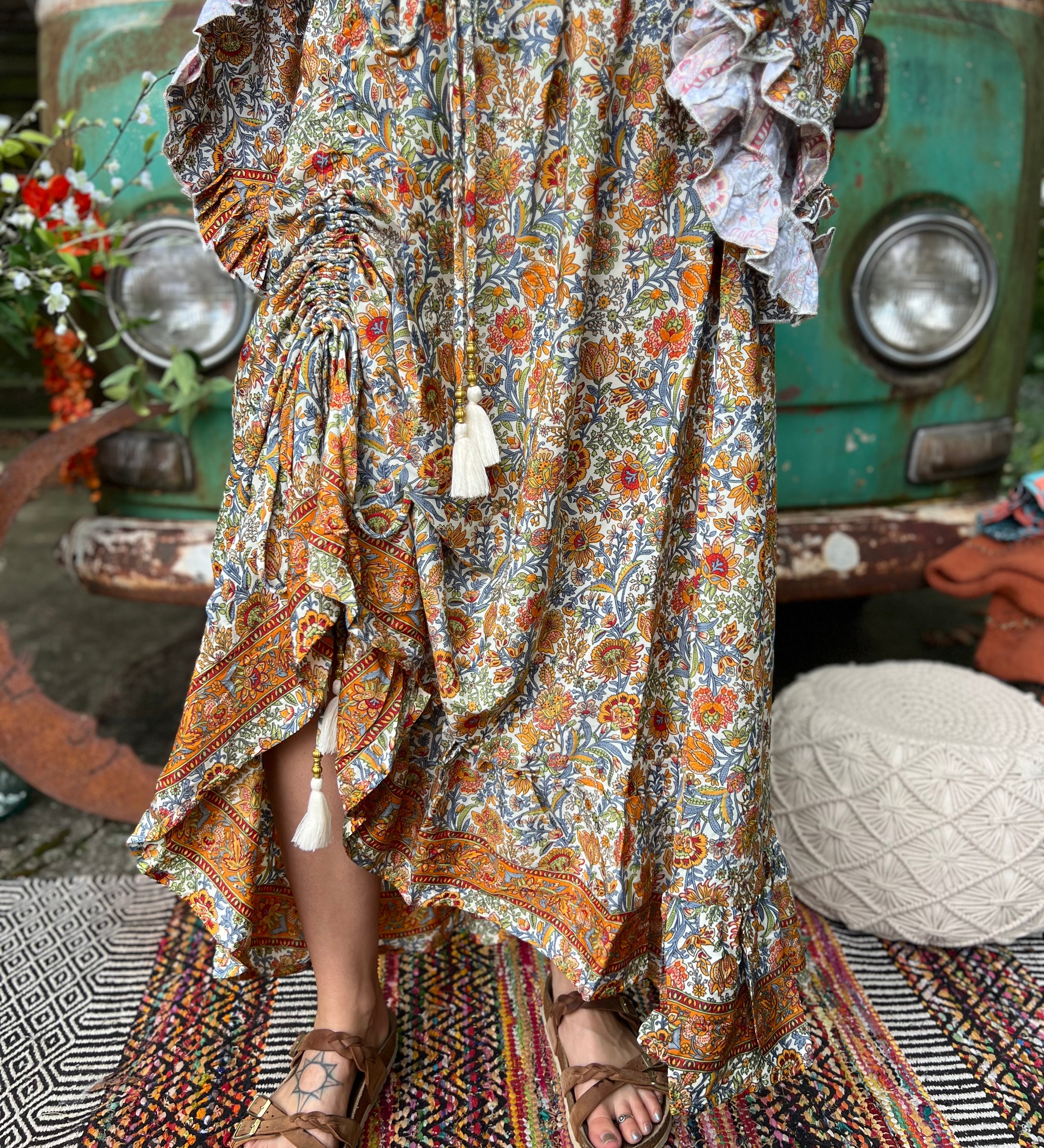 Someone wearing the orange & cream Hippie Floral Cinch Maxi Ruffle Skirt in front of a Volkswagen bus.