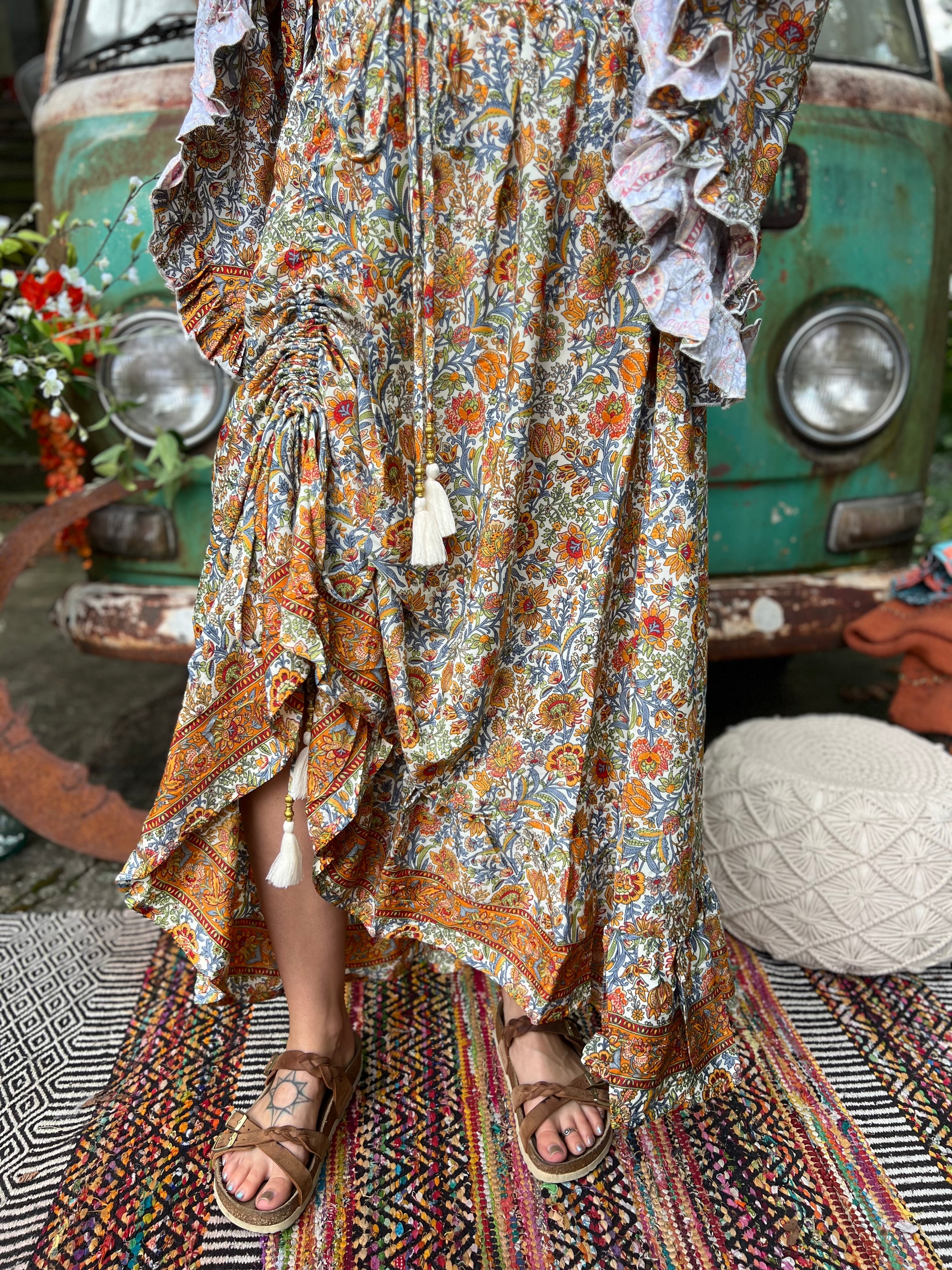 Someone wearing the orange & cream Hippie Floral Cinch Maxi Ruffle Skirt in front of a Volkswagen bus.
