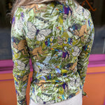 A woman wearing the green Cosmic Mythology Long Sleeve Top with beige linen pants in front of a window.