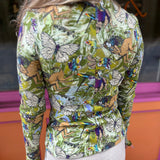 A woman wearing the green Cosmic Mythology Long Sleeve Top with beige linen pants in front of a window.