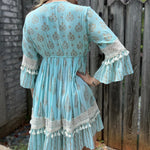 A woman wearing the Blue Crepe Thread Embroidered & Lace Decorated Dress in front of a wooden fence.