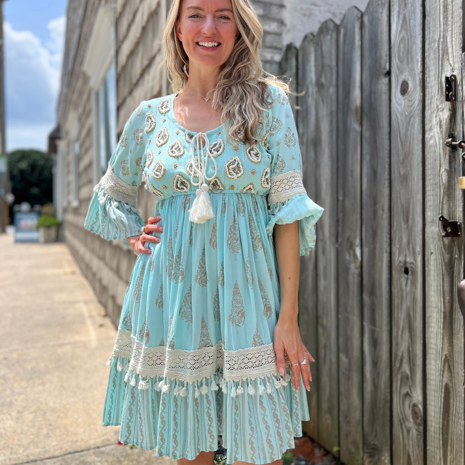 A woman wearing the Blue Crepe Thread Embroidered & Lace Decorated Dress in front of a wooden fence.