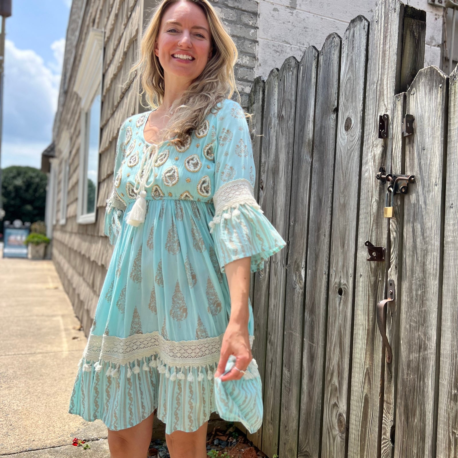A woman wearing the Blue Crepe Thread Embroidered & Lace Decorated Dress in front of a wooden fence.