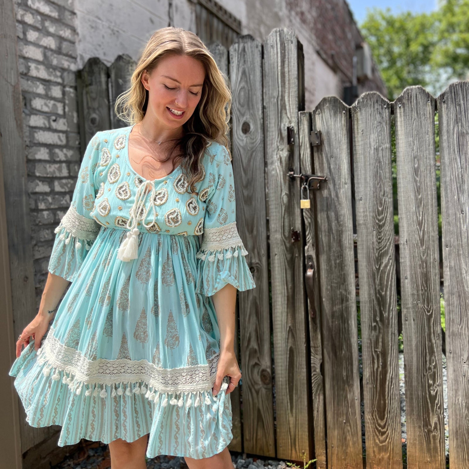A woman wearing the Blue Crepe Thread Embroidered & Lace Decorated Dress in front of a wooden fence.