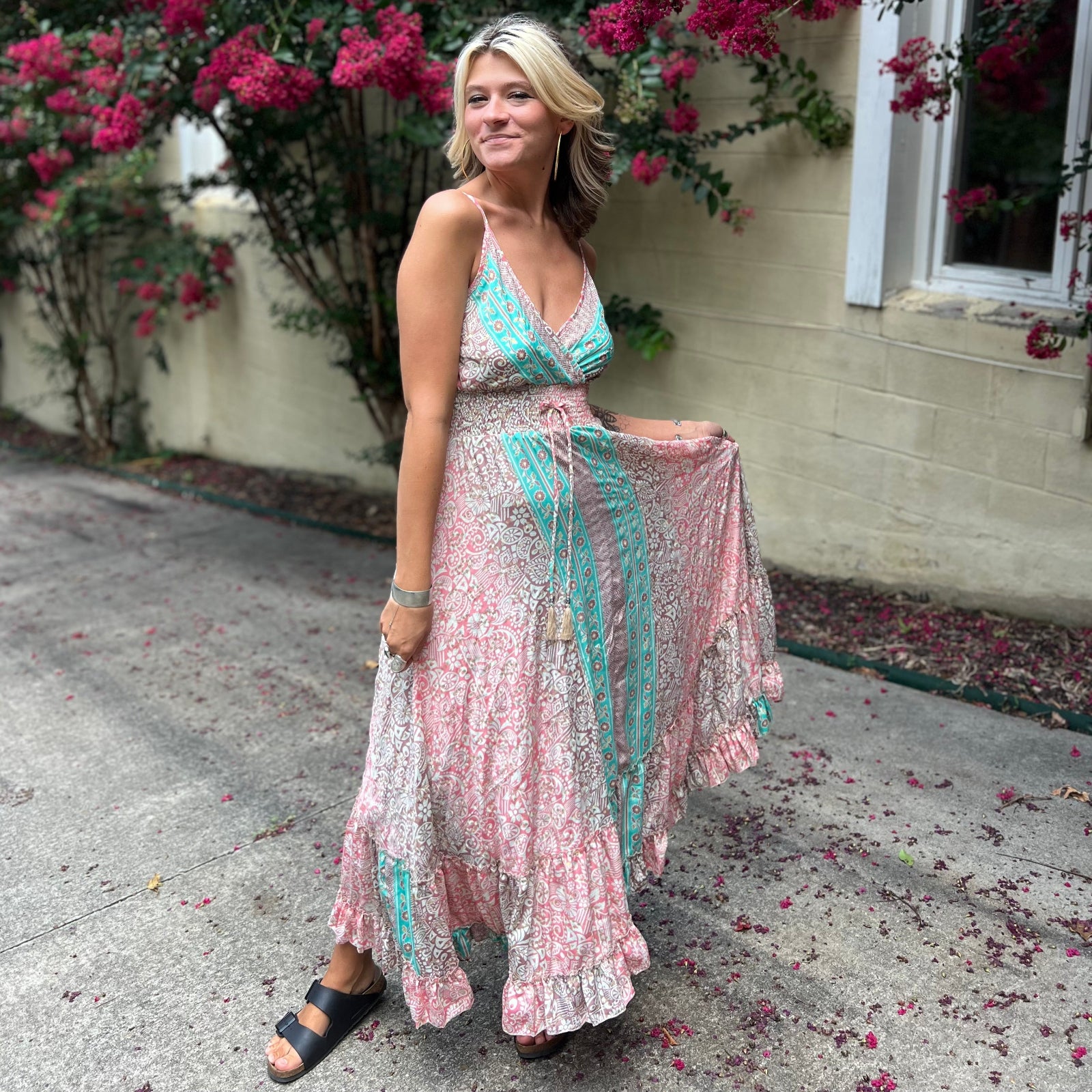 A woman wearing the Bohemian Silk Multi Pink Spaghetti Straps Halter Dress in front of a white wall with pink flowers.