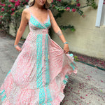 A woman wearing the Bohemian Silk Multi Pink Spaghetti Straps Halter Dress in front of a white wall with pink flowers.