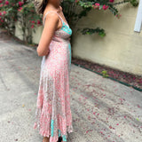 A woman wearing the Bohemian Silk Multi Pink Spaghetti Straps Halter Dress in front of a white wall with pink flowers.