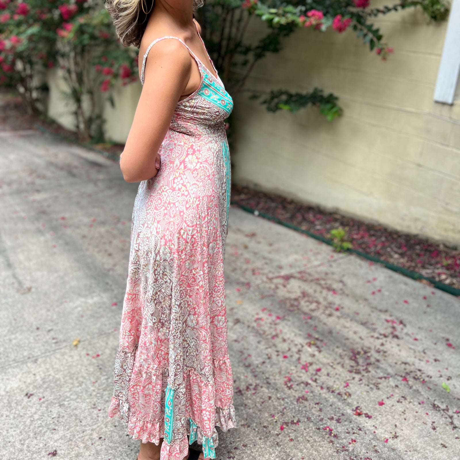 A woman wearing the Bohemian Silk Multi Pink Spaghetti Straps Halter Dress in front of a white wall with pink flowers.