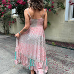 A woman wearing the Bohemian Silk Multi Pink Spaghetti Straps Halter Dress in front of a white wall with pink flowers.