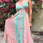 A woman wearing the Bohemian Silk Multi Pink Spaghetti Straps Halter Dress in front of a white wall with pink flowers.