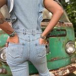 A woman wearing the Ruffle Button Up Bell Bottom Light Wash Denim Jumpsuit in front of a vintage teal Volkswagen bus.
