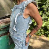 A woman wearing the Ruffle Button Up Bell Bottom Light Wash Denim Jumpsuit in front of a vintage teal Volkswagen bus.