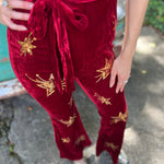 A woman wearing the burgundy Suede Sequin Embellished Embroidered Bootcut Jumpsuit in front of a teal vintage Volkswagen bus.