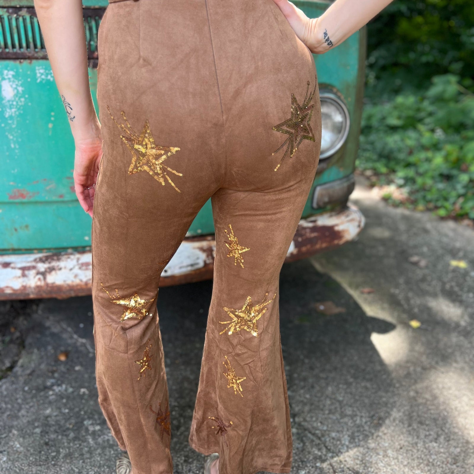 A woman wearing the camel Suede Sequin Embellished Embroidered Bootcut Jumpsuit in front of a teal vintage Volkswagen bus.