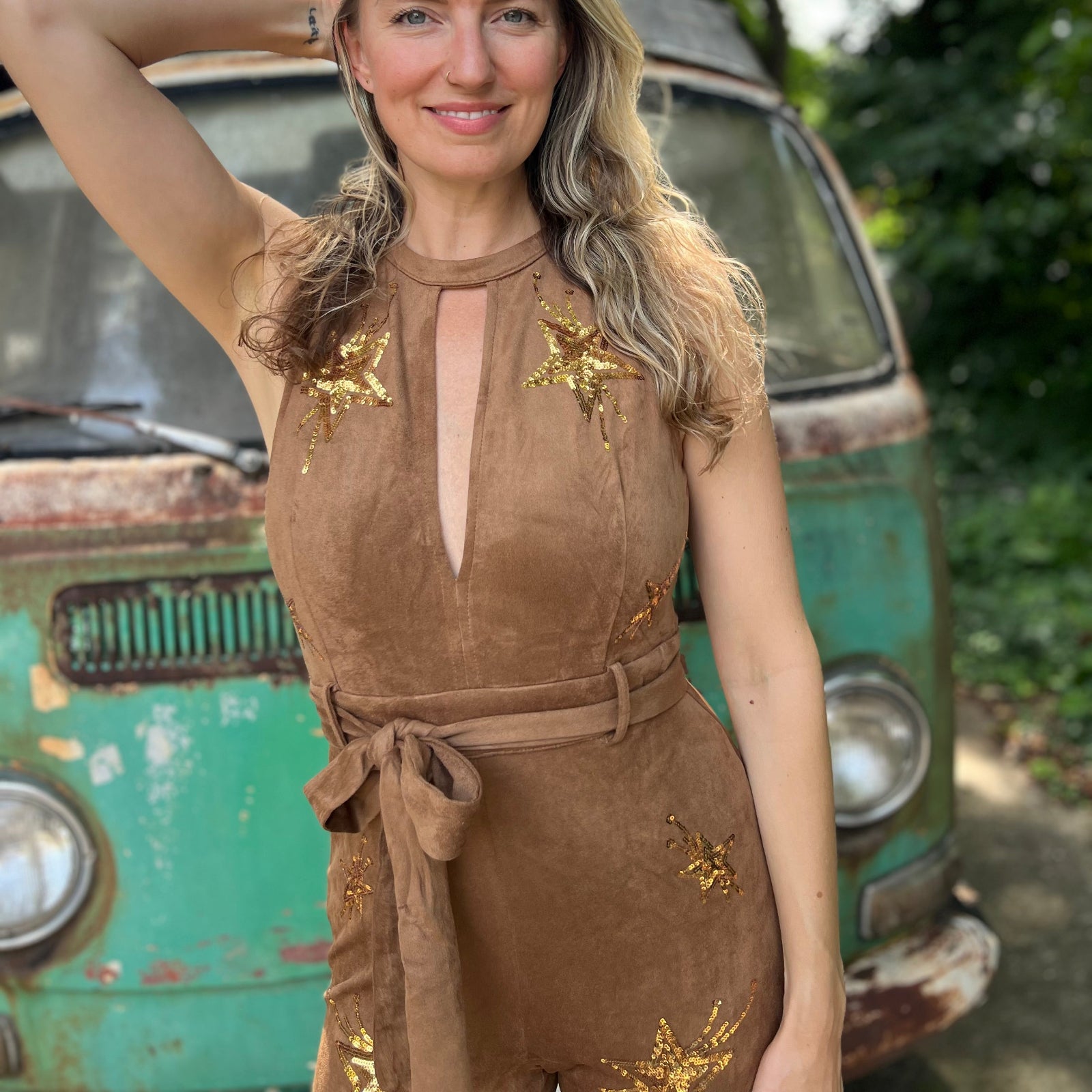 A woman wearing the camel Suede Sequin Embellished Embroidered Bootcut Jumpsuit in front of a teal vintage Volkswagen bus.