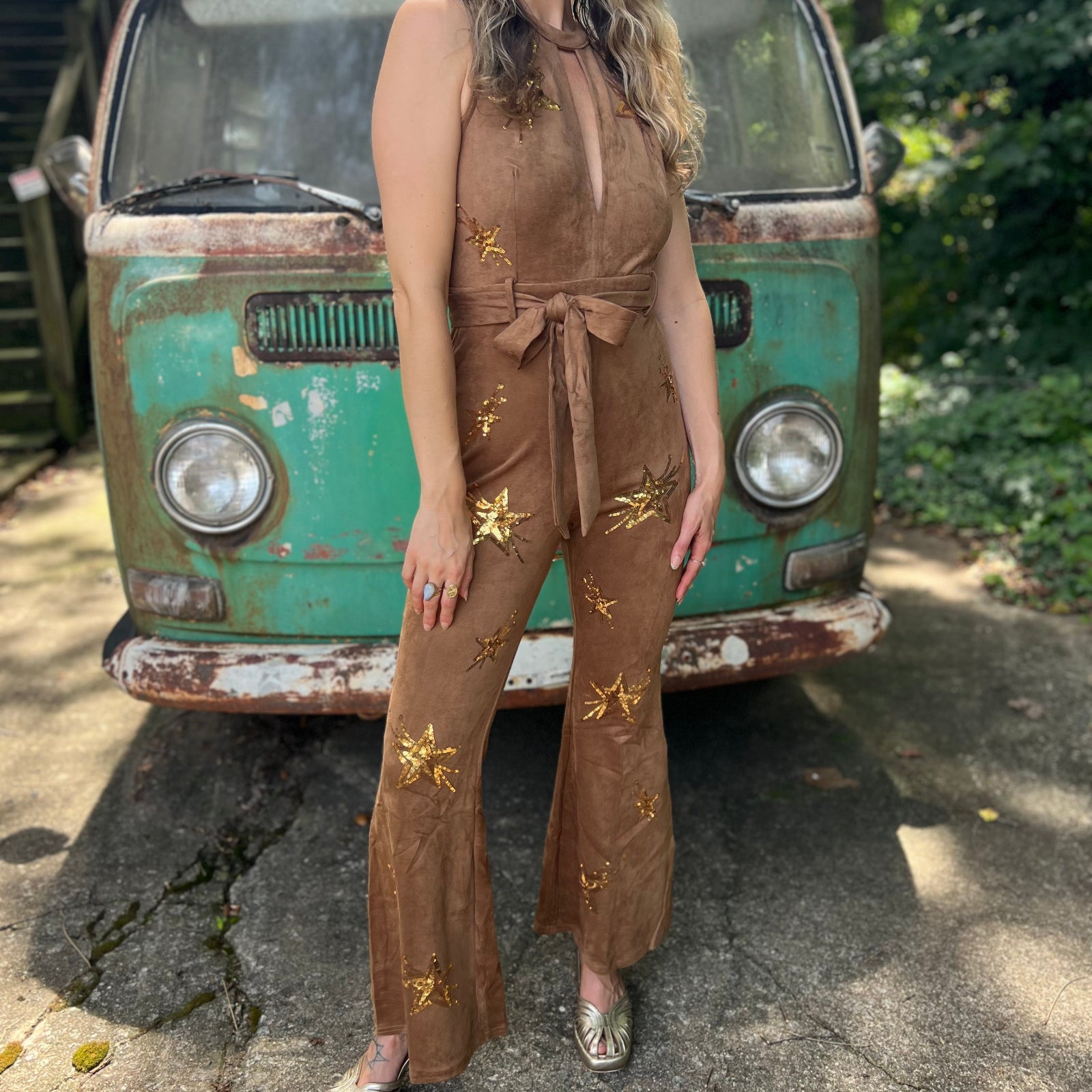 A woman wearing the camel Suede Sequin Embellished Embroidered Bootcut Jumpsuit in front of a teal vintage Volkswagen bus.