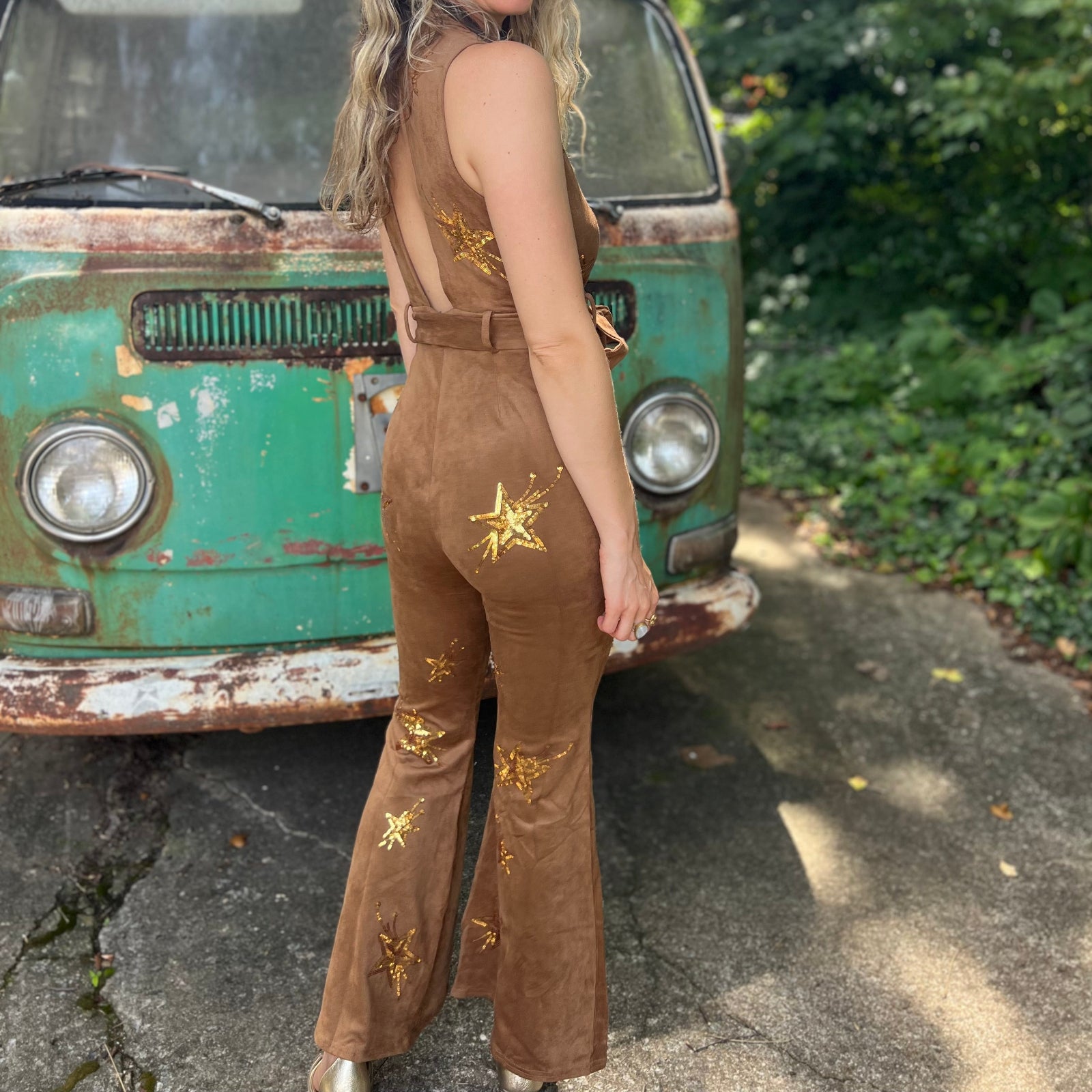 A woman wearing the camel Suede Sequin Embellished Embroidered Bootcut Jumpsuit in front of a teal vintage Volkswagen bus.