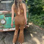 A woman wearing the camel Suede Sequin Embellished Embroidered Bootcut Jumpsuit in front of a teal vintage Volkswagen bus.
