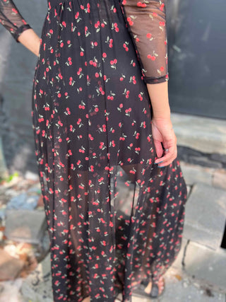 Back close up view of a woman wearing a black mesh cherry print maxi dress, showing the sheer detail and attached slip.