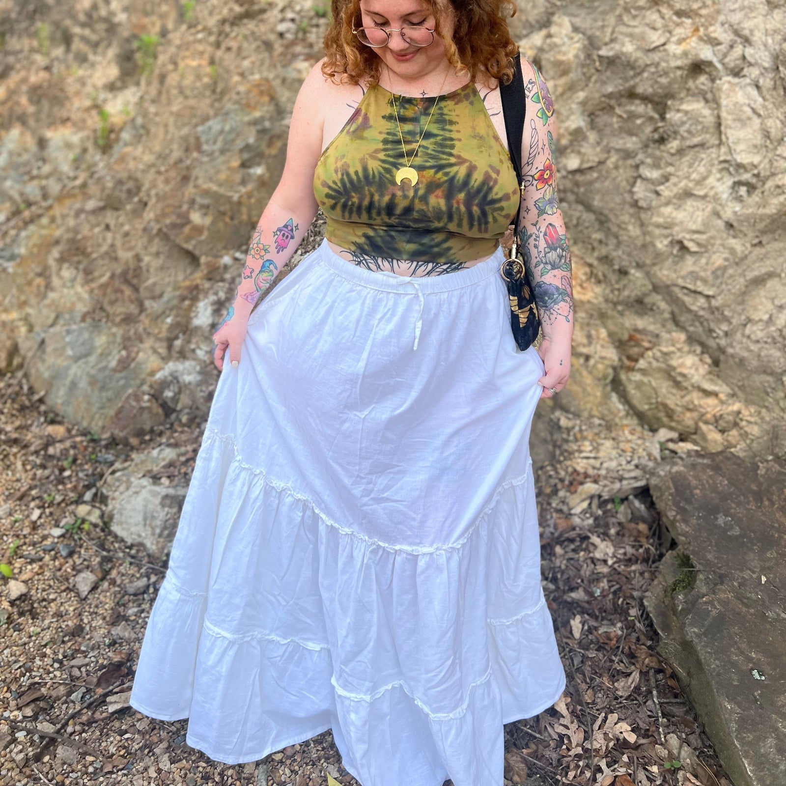 A woman wearing a tie dye top with the white Homespun Tiered Maxi Skirt in front of a rock wall.