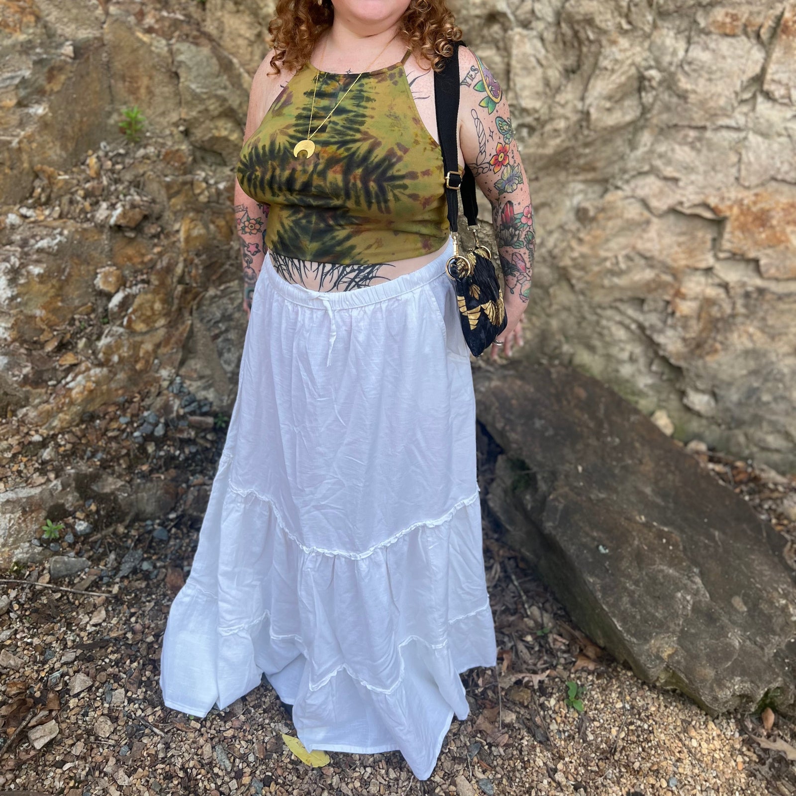 A woman wearing a tie dye top with the white Homespun Tiered Maxi Skirt in front of a rock wall.
