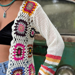 An up-close image of someone wearing the Bohemian Rainbow Crochet Cardigan in front of an old teal Volkswagen bus.