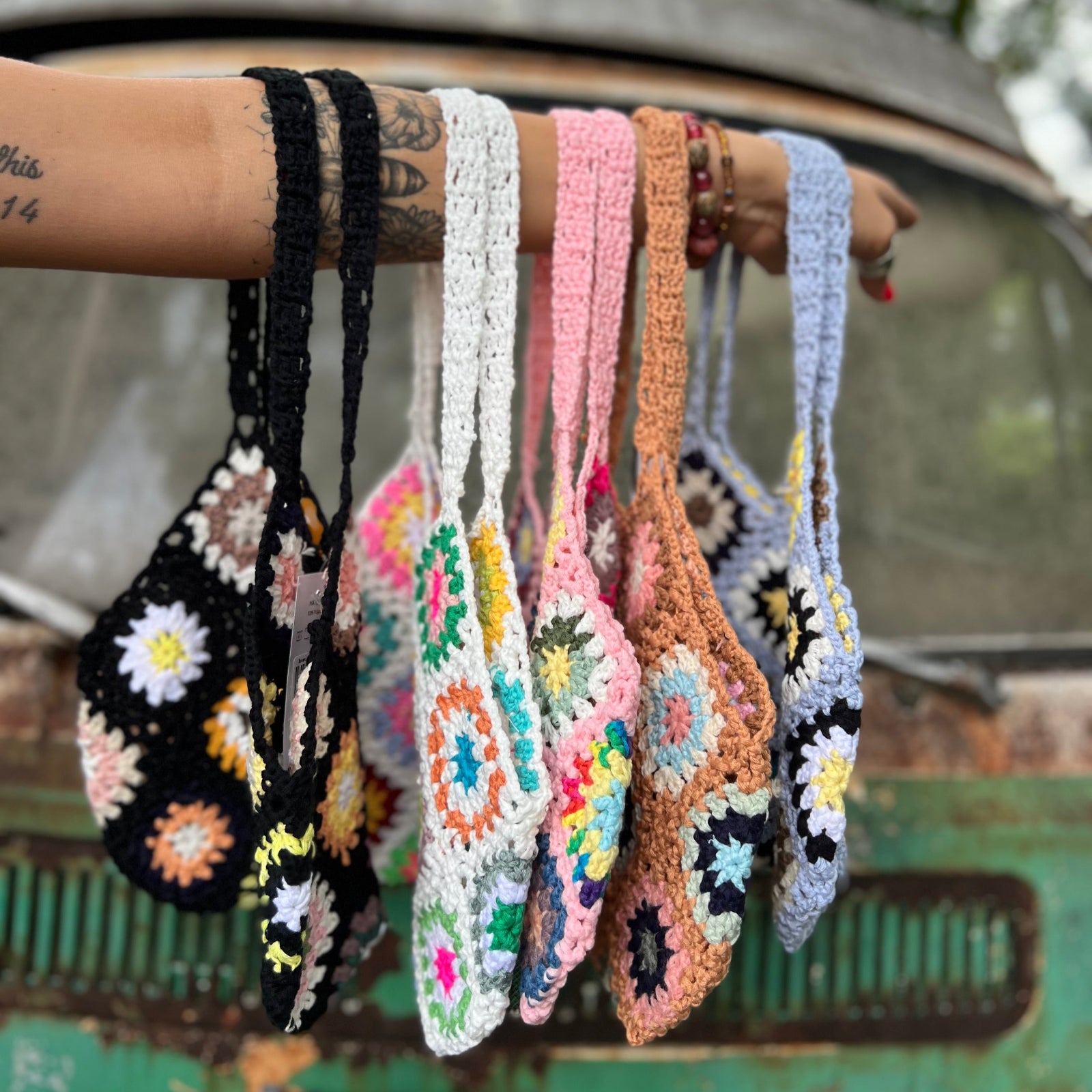 All varieties of the Bohemian Handmade Crochet Bags on an arm in front of an teal Volkswagen bus.
