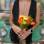 A woman wearing the black Western Open Soft Suede Fringe Vest and animal print pants while holding flowers.