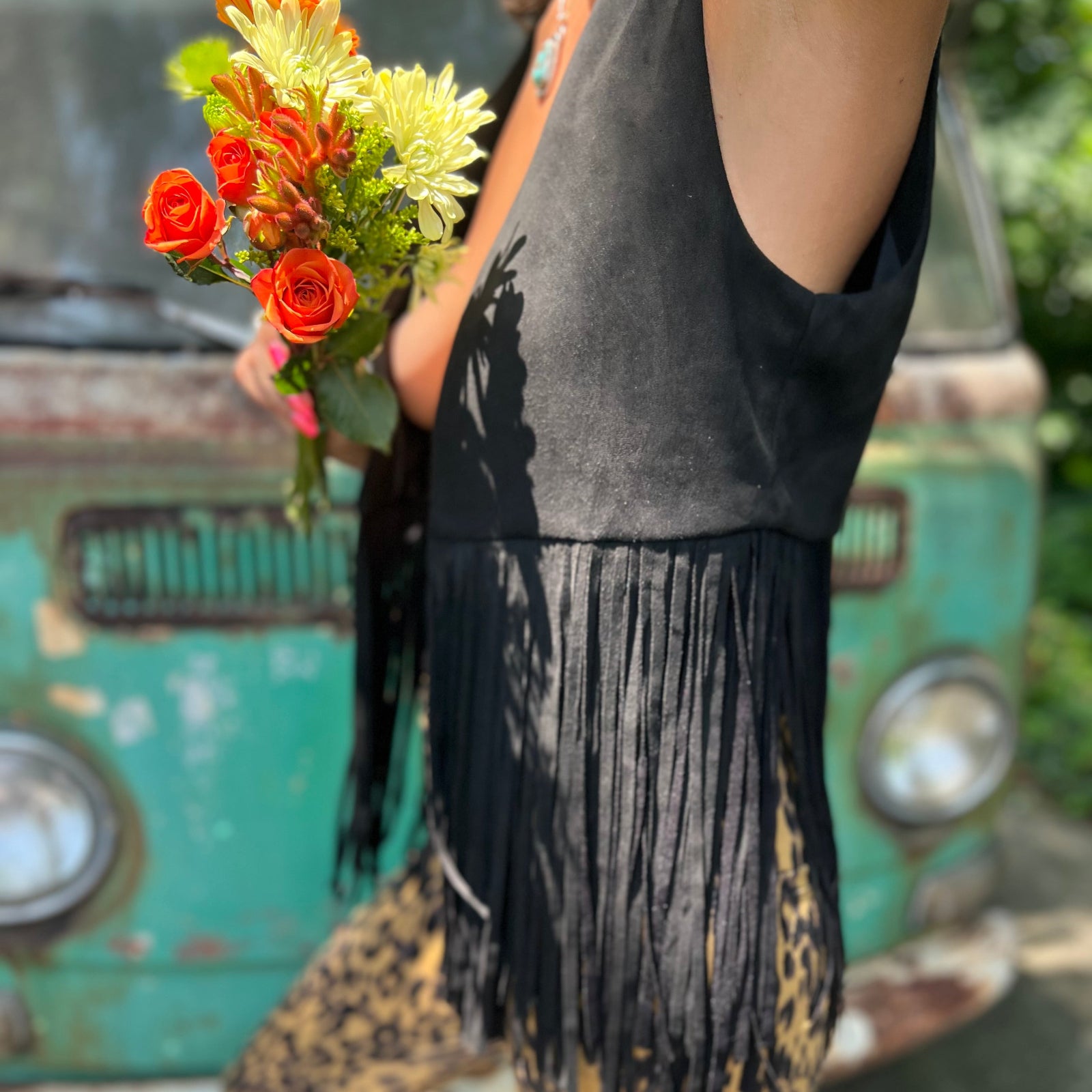 A woman wearing the black Western Open Soft Suede Fringe Vest and animal print pants.