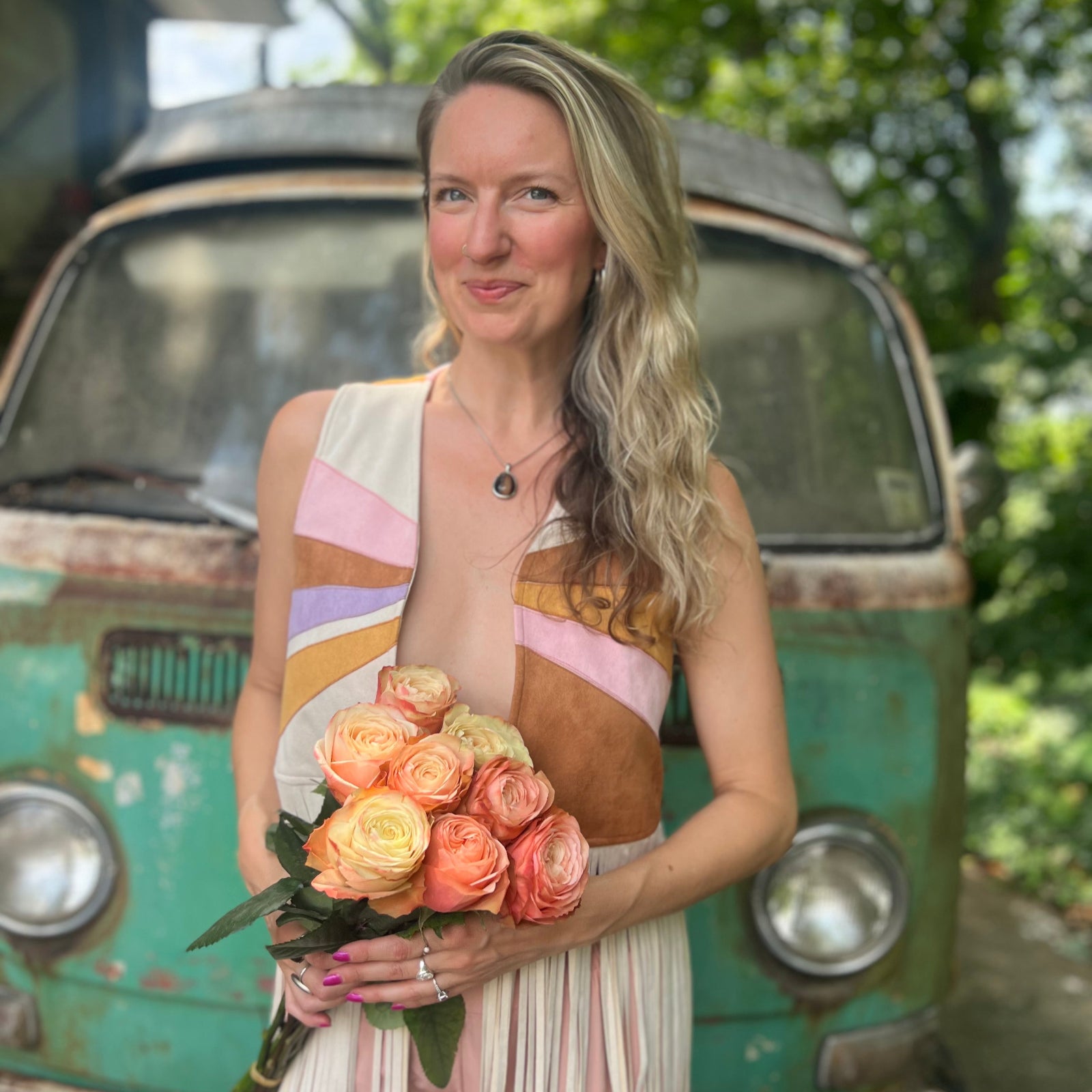 A woman wearing the cream Retro Sunburst Suede Color Block Long Fringe Faux Vest and holding a bouquet.