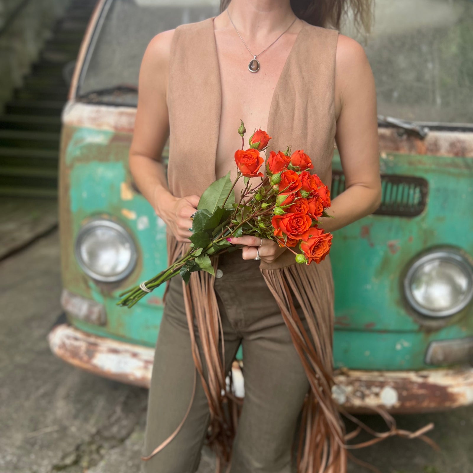 A woman wearing the tan Faux Suede Long Fringe Western Vest while holding flowers.